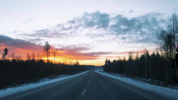 View Through the Windshield of a Moving Car on the Road in Winter and a Beautiful Sunrise in the Sky