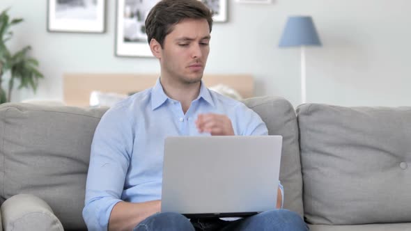 Handsome Young Man Thinking and Working on Laptop While Sitting on Couch