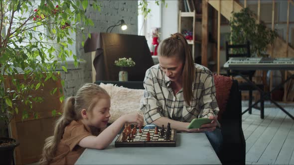 A Woman and a Girl are Sitting at a Table in the Living Room and Playing Chess