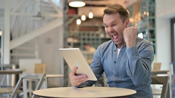 Casual Man Celebrating Success on Tablet in Cafe