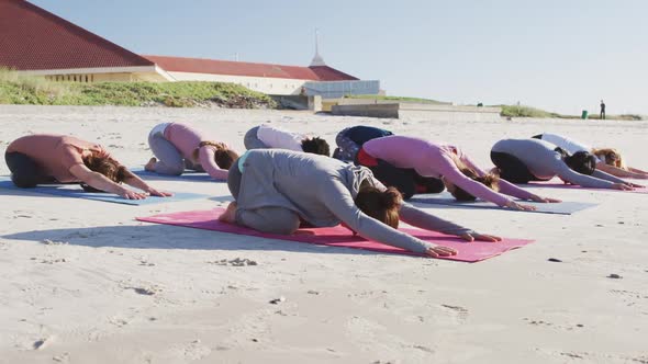 Multi-ethnic group of women doing yoga position on the beach and blue sky background