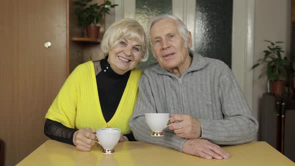Happy Old Grandparents Couple Sit on Table at Home Enjoy Drinking Tea Together