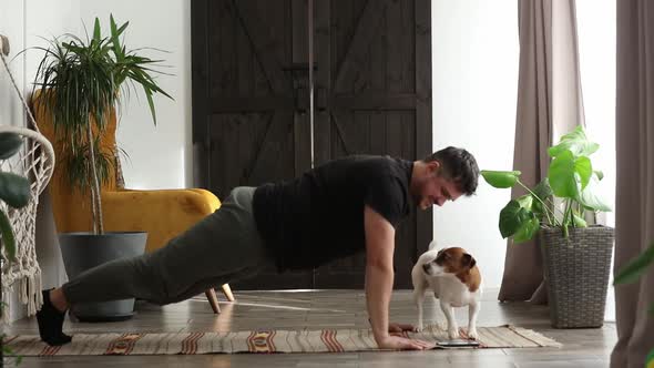 man trying to do sports exercises with a dog at home on the floor