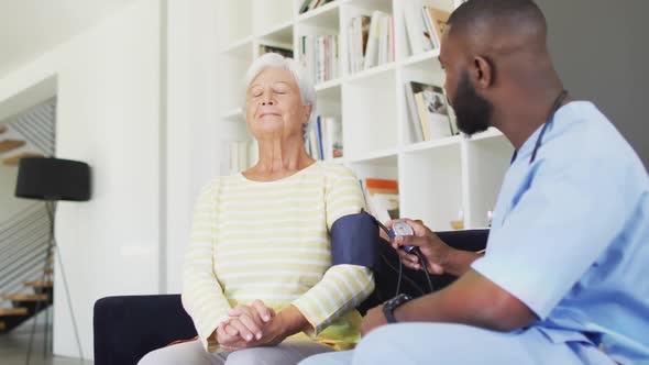 Video of happy african american male doctor checking pressure to caucasian senior woman