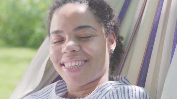 Close-up Face of Adorable Happy African American Woman Lying in the Hammock, Relaxing in the Garden