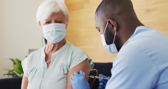 Video of african american male doctor in face mask vaccinating caucasian senior woman