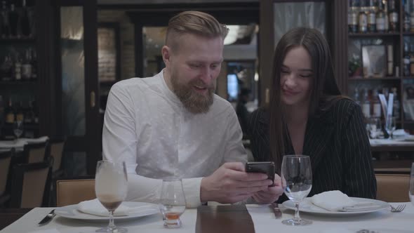 Blonde Bearded Man and Brunette Woman Sitting in the Restaurant at the Table