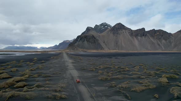 Drone video of Stokksnes Vestrahorn black sand beach in Iceland with Red car driving down dirt road