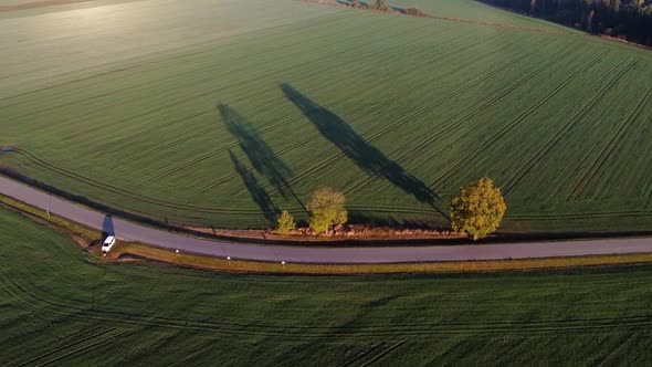 Drone flying over a small country road with green farming fields and beautilfu shadows of the trees