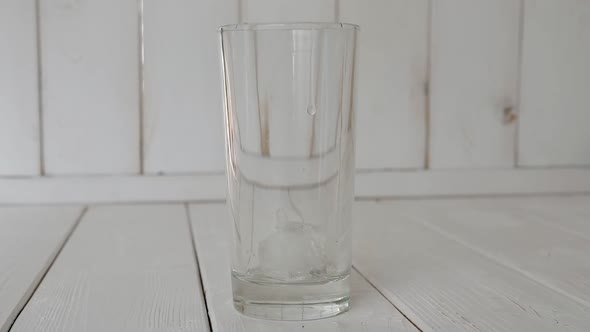 Closeup of Ice Cubes Falling Into an Empty Glass on a Light Wooden Background