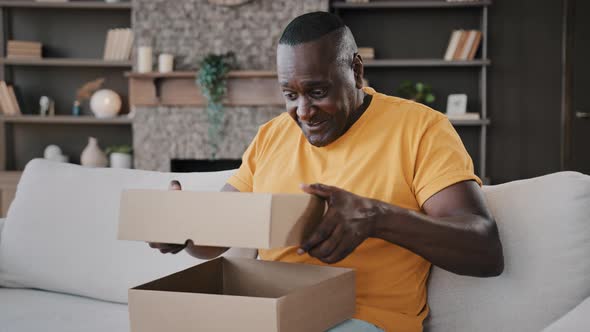 Happy Surprised African Senior Man Open Cardboard Box with Gift Unpacking Parcel Delivery Internet