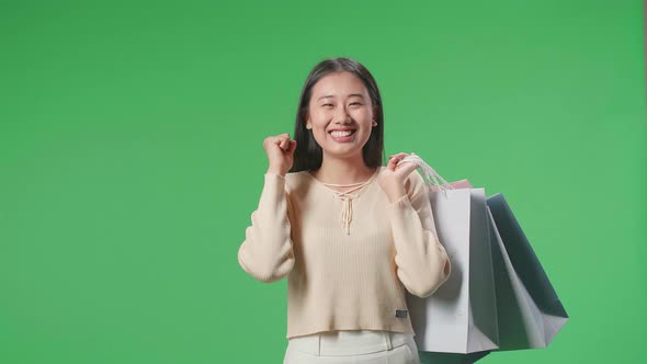 Woman Holding Shopping Bags Up Being Happy And Smiling While Standing In Front Of Green Screen