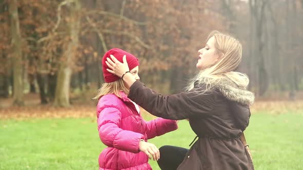 Mother putting cap on daughter's head and kissing her in forehead