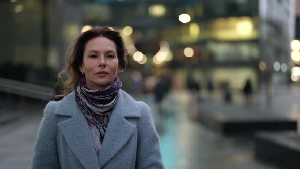 Portrait of a Woman in a Light Coat and Scarf at Dusk Against a Background of Blurred Lights