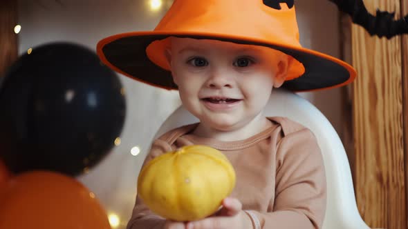 Portrait of Baby Boy Wearing Halloween Hat and Holding Little Pumpkin