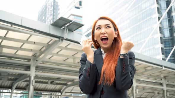 Young Asian Business Woman is Shocked and Surprised While Holding Smart Phone in Urban City