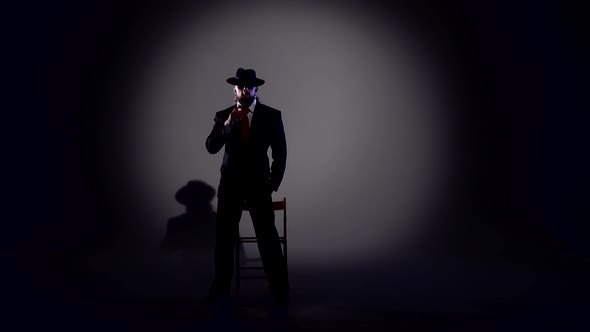 Elegant Man in a Black Hat Is Dancing an Erotic Dance. Spotlight on a Black Background.