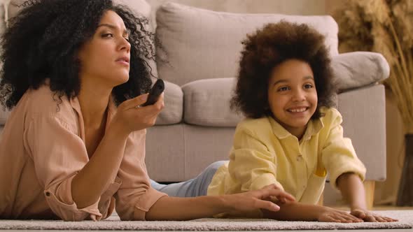 African American Woman and Litle Girl Watching TV Switching Channels with Remote Control