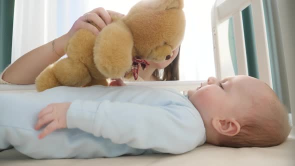 Little Boy Looking and Reaching for Teddy Bear in His Cradle