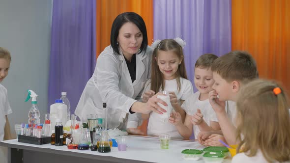 Chemical Experiments for Children. Woman Pours a Green Substance Into a Clear Glass. Children Are