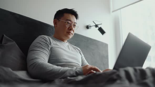 Smiling Asian man wearing eyeglasses working on laptop