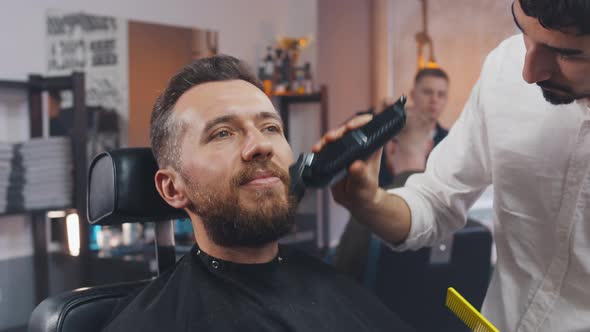 Professional Barber Trimming Man's Beard with Electric Razor