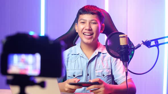 Excited Asian Kid Boy Playing Video Game With Mobile Phone Then Smiles To Camera While Live Stream