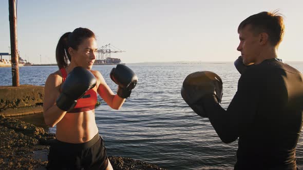 Young Woman in Boxing Gloves and Sportswear is Practicing on a Boxing Paw with Her Skillful Coach