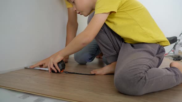 Father and His Little Son Install Laminate on the Floor in Their Apartment