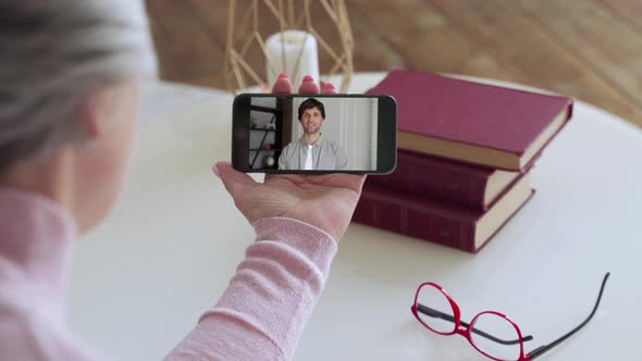 Over the Shoulder View of an Elderly Woman Video Call To a Young Son Using a Smartphone. The Concept