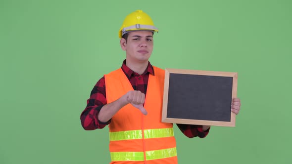 Stressed Young Multi Ethnic Man Construction Worker Holding Blackboard and Giving Thumbs Down