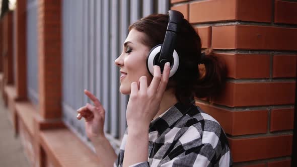 Beautiful Brunette Leaning on a Brick Fence Outdoors Listening to Music on Headphones with Eyes