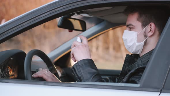Man in a Disposable Mask Is Spraying Antiseptic on the Car's Steering