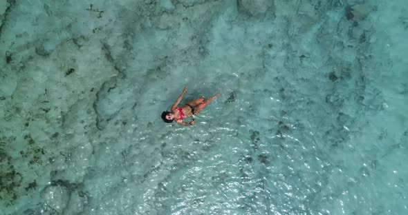 Young Caucasian woman wearing bikini bathing suit floating in crystal clear green ocean water lookin