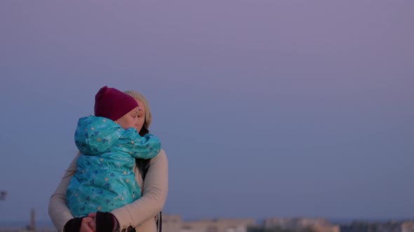 Mother and daughter standing on evening city lanscape. A little girl hugging and kissing mom