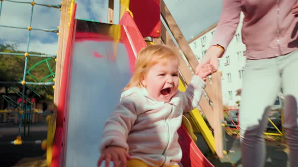 A happy little baby is rolling down a children's slide.