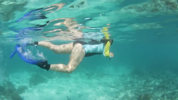 A girl in a swimming costume snorkelling in tropical waters while using an underwater camera