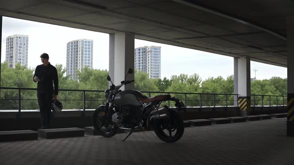 Motorbike Driver Standing at the Parking Lot Looking at Phone Forest Behind Him