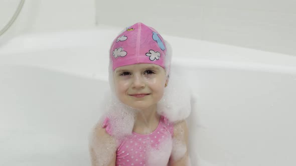 Cute Blonde Girl Takes a Bath in Swimwear. Little Child Washes Her Head