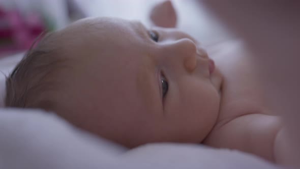 Closeup Side View Portrait Curios Infant Lying in Bed Looking Around Moving Hands