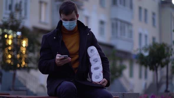 Men Sits on Bench in Medical Mask with Toilet Paper and Smartphone During the Second Wave Quarantine