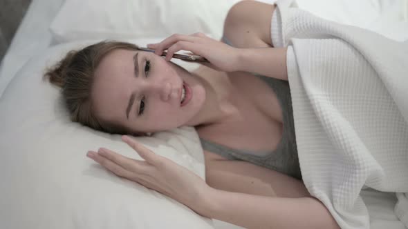 Angry Young Woman Talking on Smartphone in Bed