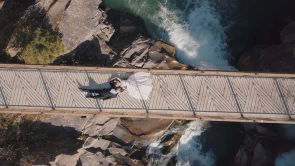 Newlyweds. Bride and Groom Lie on a Bridge Over a Mountain River. Aerial View