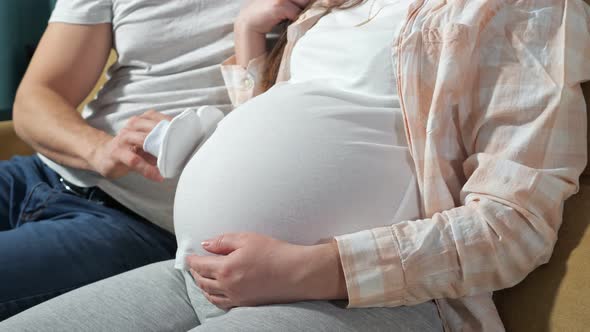 Unrecognizable Man Plays with Booties on Fingers with a Baby in the Belly of Pregnant Wife