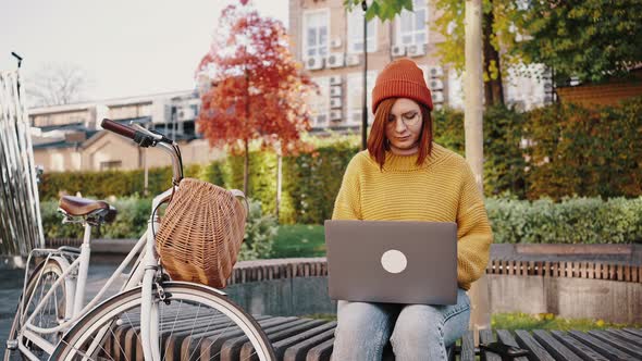 Young Female Sitting on Bench in City Park Working Online on Laptop