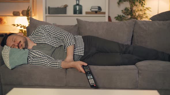 Portrait of Tired Person Sleeping on Couch Alone Holding TV Remote Control