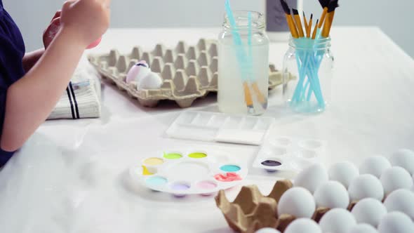 Little girl painting craft Easter eggs with acrylic paint