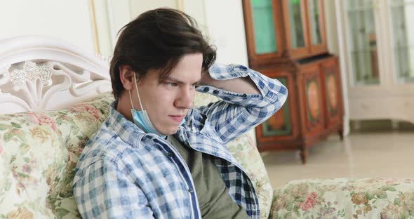 Sad Boy with Medical Mask Bored on Sofa Corrects Hairstyle and Thinks at Home