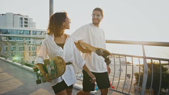 Tracking Shot of Millennial Couple of Skaters Walking with Skateboards and Flirting