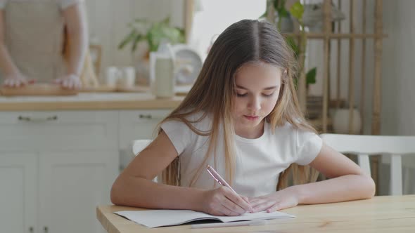 Teenager Girl Child Schoolgirl Pupil Sitting at Home at Table in Kitchen Doing Homework Writing